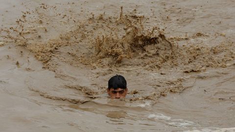 Un joven pakistaní trata de nadar en medio de la riada causada por las fuertes lluvias en la localidad de Charsadda
