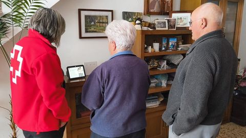 Una voluntaria de la Cruz Roja muestra el funcionamiento del dispositivo electrónico a dos personas mayores