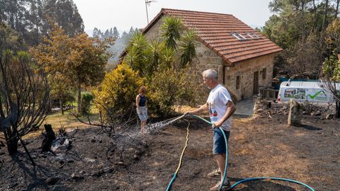 Mari Pereira y su marido refrescan con agua la parcela calcinada que rodea su casa
