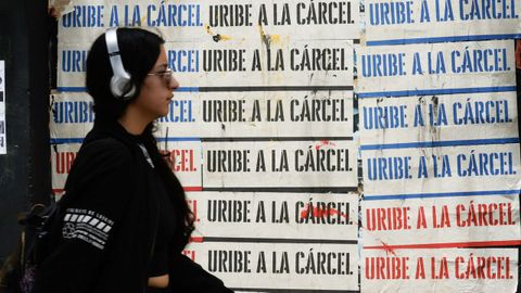 Una mujer pasa cerca de varios carteles, colocados en la ciudad de Bogot, en los que se pide la entrada en prisin del expresidente lvaro Uribe.