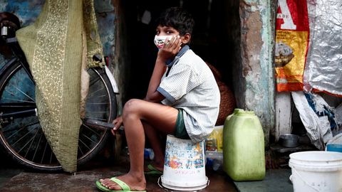 Un nio que lleva una mscara facial protectora se sienta en un balde afuera de una casa en una zona de tugurios, durante un bloqueo nacional prolongado para frenar la propagacin de la enfermedad por coronavirus, en Nueva Delhi, India