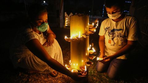 Los devotos budistas de Sri Lanka, con mascarillas, encienden lámparas de aceite durante las celebraciones religiosas del día de luna llena de Poson en un templo