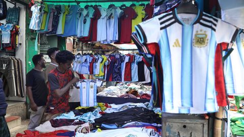 Varios hombres miran camisetas de las selecciones de f&uacute;tbol del Mundial en un puesto callejero situado en Dhaka, Bangladesh.