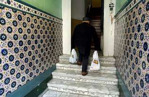 Un anciano cargado con bolsas de la compra enfila las escaleras de su portal