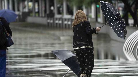 Una mujer se intenta proteger de la lluvia y el viento con un paraguas, este mircoles en el paseo de la playa de San Lorenzo en Gijn