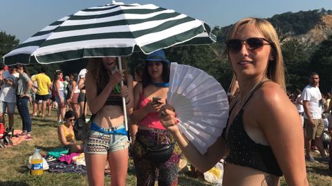 Una joven se abanica contra el calor mientras dos amigas se ocultan del sol con una sombrilla en Pola de Siero. Carm�n