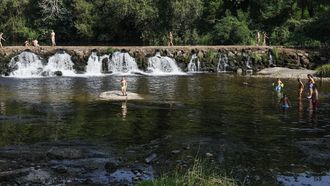 Varias personas, la mayora nios, se refrescan en el rea recreativa A Veronza, en el ro Avia