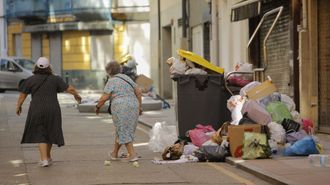 Dos mujeres rodean la basura para avanzar por una calle de Os Mallos durante la huelga del 2024