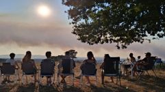 En la foto, un grupo de turistas belgas sigue el eclipse el mi�rcoles en Taboada, con el cielo medio cubierto por el humo de este incendio