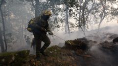 Un bombero forestal de la brigada de Melide trabaja con un irrigador de agua en el incendio de Pantn