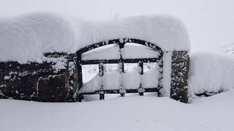 La puerta de una verja completamente cubierta de nieve en Pajares