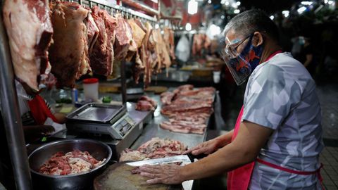 Un vendedor utiliza mascarilla y protecci�n facial mientras que corta carne en un mercado en Ciudad Quez�n, Filipinas