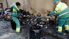 Dos trabajadores retiran residuos tras el incendio de contenedores en la calle Marconi de A Corua durante la huelga del 2024