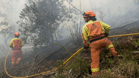 Unos bomberos trabajan en las labores de extinción del incendio declarado en Navelgas, en Asturias