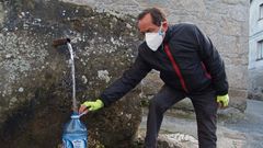Un vecino de Chantada coge agua de una fuente provisto de mascarilla
