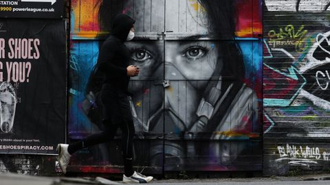 Un hombre con una mscara protectora corre por delante de un graffiti en Brick Lane, en Londres