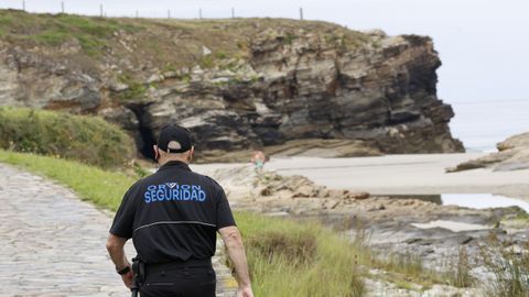 Un vigilante dirigi�ndose a la zona acordonada para impedir el paso, con la playa vac�a en un d�a de lluvia