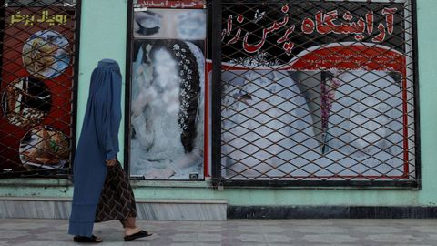 Una afgana pasa por una tienda de Kabul con una publicidad con el rostro de una mujer borrado.