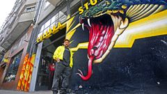 El grafitero O?Ras, en la puerta de su tienda de Pontevedra, Culebra Studio, con uno de sus grafitis de fondo