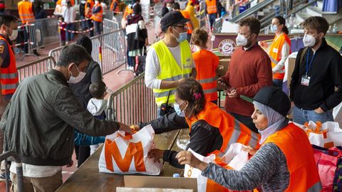 Voluntarios distribuyen alimentos a los más necesitados en Ginebra, Suíza, cumpliendo con el distanciamiento y las mascarillas