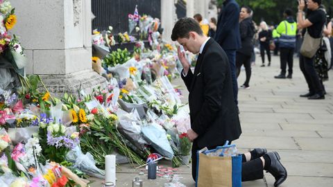 Un hombre arrodillado en frente al palacio de Buckingham, que se ha llenado de flores y mensajes en honor a Isabel II.