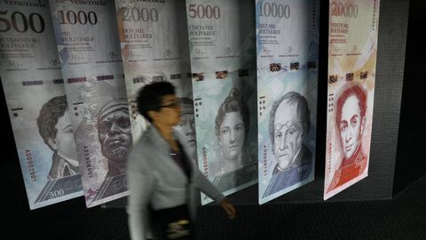 Una mujer pasa por un muestrario de los nuevos billetes de bolvares que se exhibe en la sede del Banco Central de Venezuela