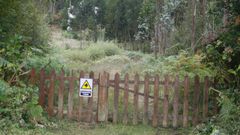 Valla de acceso a la casa okupada en Fazouro, con la vivienda al fondo, entre los �rboles