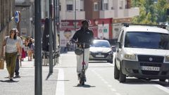 El usuario de un patinete, circulando por el carril-bici con coches aparcados.