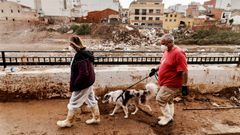 Dos personas pasean a un perro en una zona afectada por la dana en Paiporta.