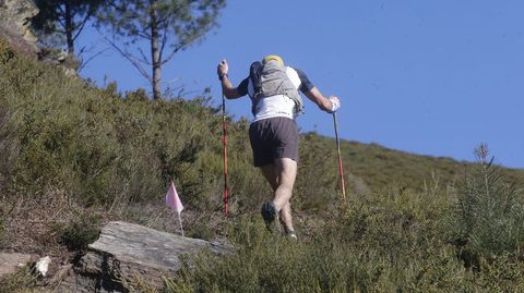 Un corredor se apoya en unos bastones de trail en un tramo complicado