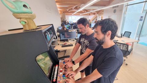 Dos empleados jugando a los marcianitos con el mueco de baby Yoda expectante