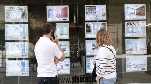 Dos personas mirando ofertas de pisos en el escaparate de una inmobiliaria de Lugo