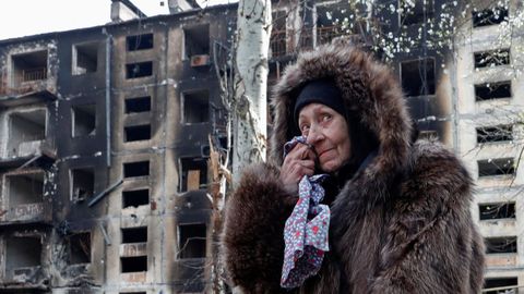 Una mujer se seca una lgrima frente a un edificio bombardeado