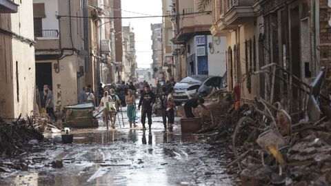 Varias personas caminan entre el lodo acumulado en las calles a causa de las intensas lluvias cadas por la fuerte dana