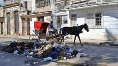 Un hombre en un carromato pasando ante la basura acumulada en una calle de Cuba