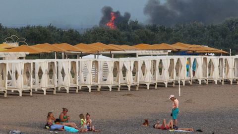 Veraneantes toman el sol en una playa de Crimea con el incendio, al fondo, de la base a�rea rusa