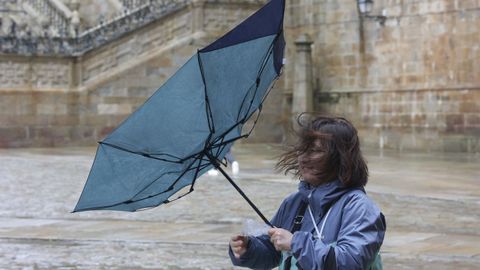 Una mujer sujeta su paraguas, doblado por el viento, en Santiago.