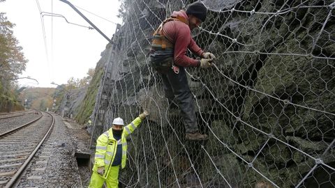 Dos operarios protegen con una malla metlica un talud sobre la va