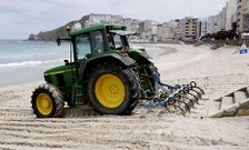 Un tractorista allana con la ayuda de una grada la arena de la playa urbana de Malpica.