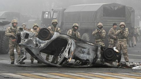 Antidisturbios se parapetan tras uno de los veh�culos incendiados en Almaty.