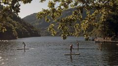 Turistas reman en unas tablas de surf frente a la playa fluvial de A Cova, en el rio Mio entre Chantada y O Saviao