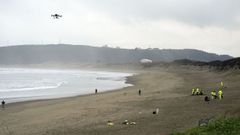 Operarios con aspiradores y con un dron en labores de limpieza en la playa asturiana de Salinas