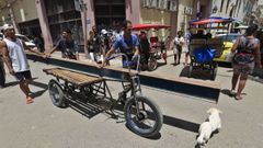 Tres hombres transportan una  viga de metal en un triciclo por las calles de La Habana