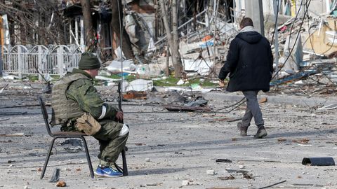 Un miembro de las tropas rusas se sienta en una silla en una calle cerca de un edificio