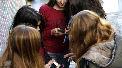 Estudiantes usando el tel&eacute;fono m&oacute;vil a la salida del colegio.