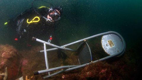 Un buzo saca una silla del fondo del puerto de Cudillero