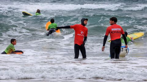 Dos monitos con un grupo de surfistas en la playa de San Lorenzo en Gijn