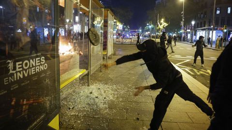 Un joven apedrea una marquesina durante los disturbios en Barcelona.