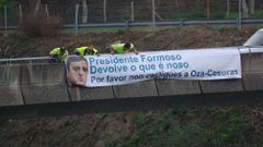 Operarios del Ayuntamiento de Oza-Cesuras colocan una de las pancartas sobre la A-6