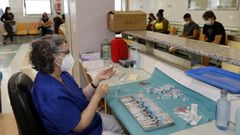 Una sanitaria prepara dosis de la vacuna contra el covid en el Hospital P�blico da Mari�a mientras varios j�venes esperan tras recibir la vacuna